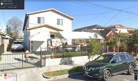 A green car is parked in front of a white house.