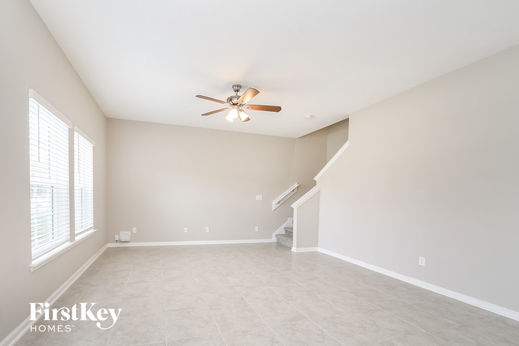 an empty living room with a ceiling fan and a staircase
