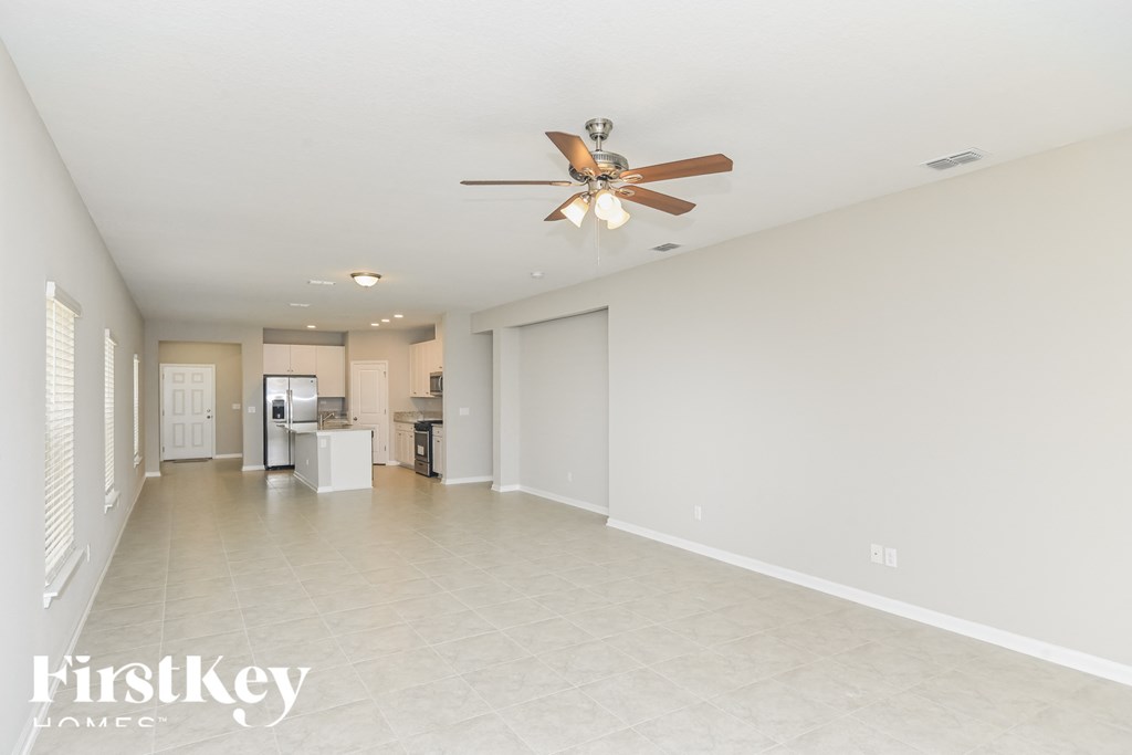 A spacious, empty room with a ceiling fan and a refrigerator in the background.