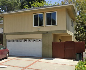 A tan house with a red car in front.