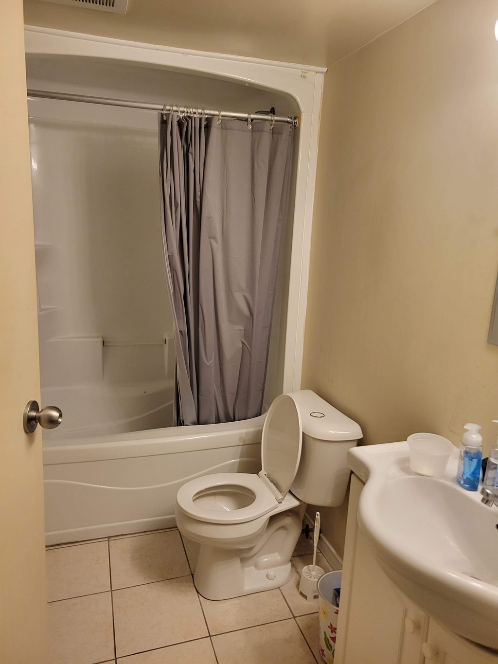 A white toilet with a grey shower curtain in the background.