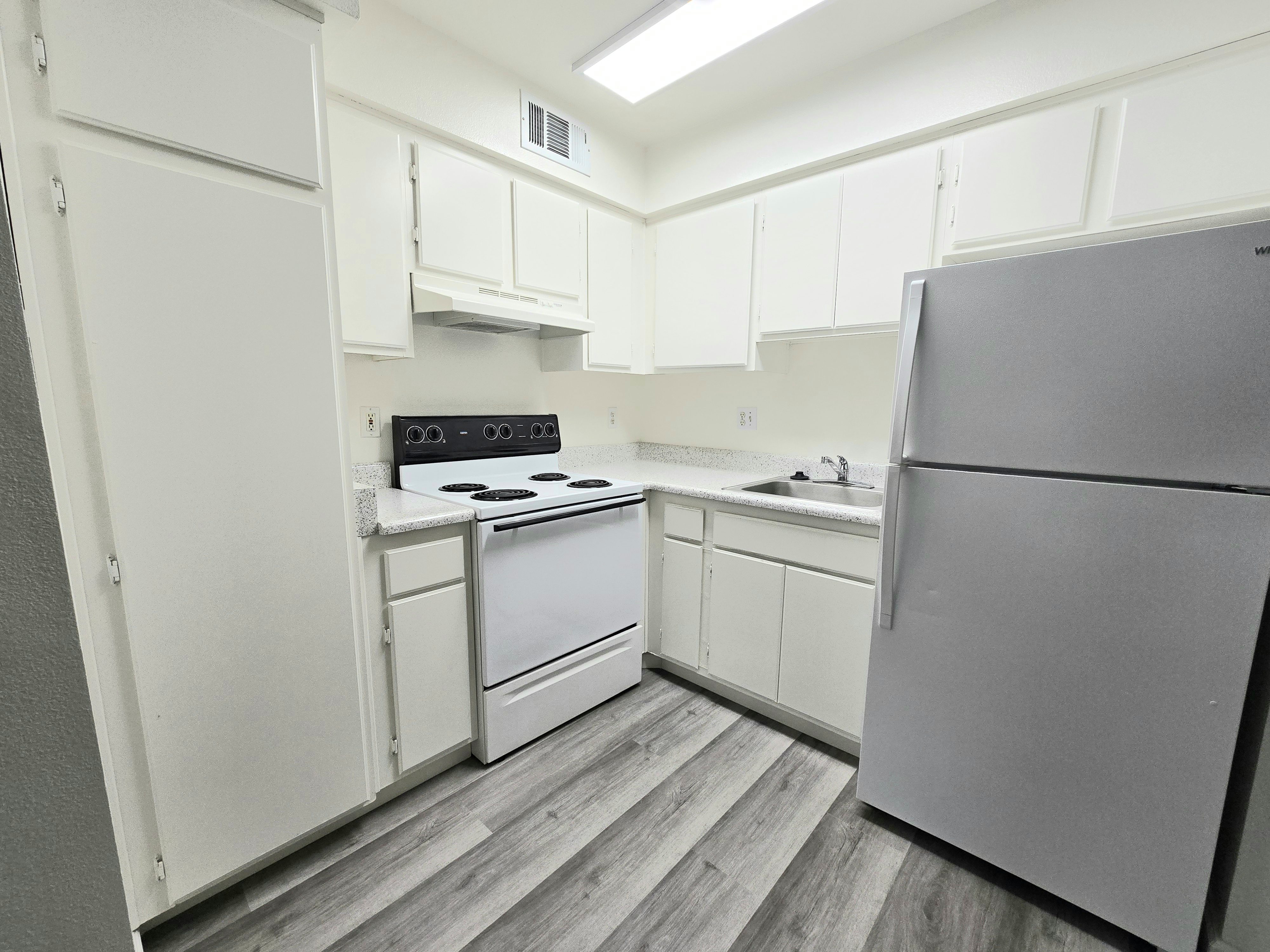 A kitchen with white cabinets and a grey fridge.