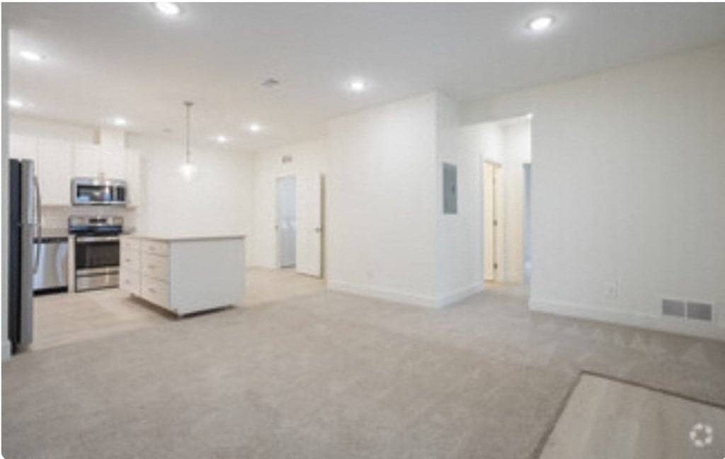 an empty living room with a kitchen in the middle of it