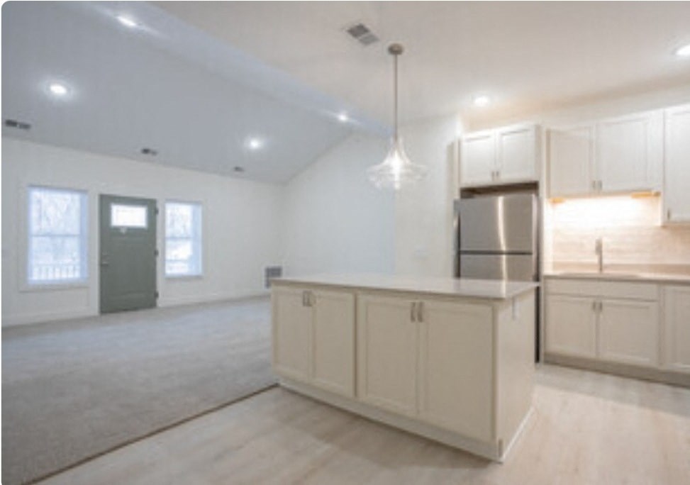 an empty living room with a kitchen with white cabinets