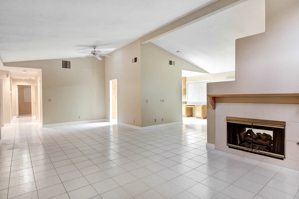 A large, empty room with a fireplace and a ceiling fan.