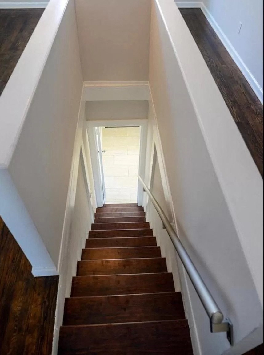 a view down the stairs of a house with white walls and wood floors