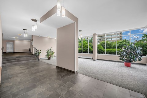 A spacious room with a grey floor and a large window overlooking a green area.