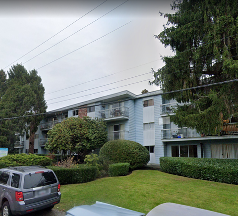 A grey car is parked in front of a blue and white apartment building.