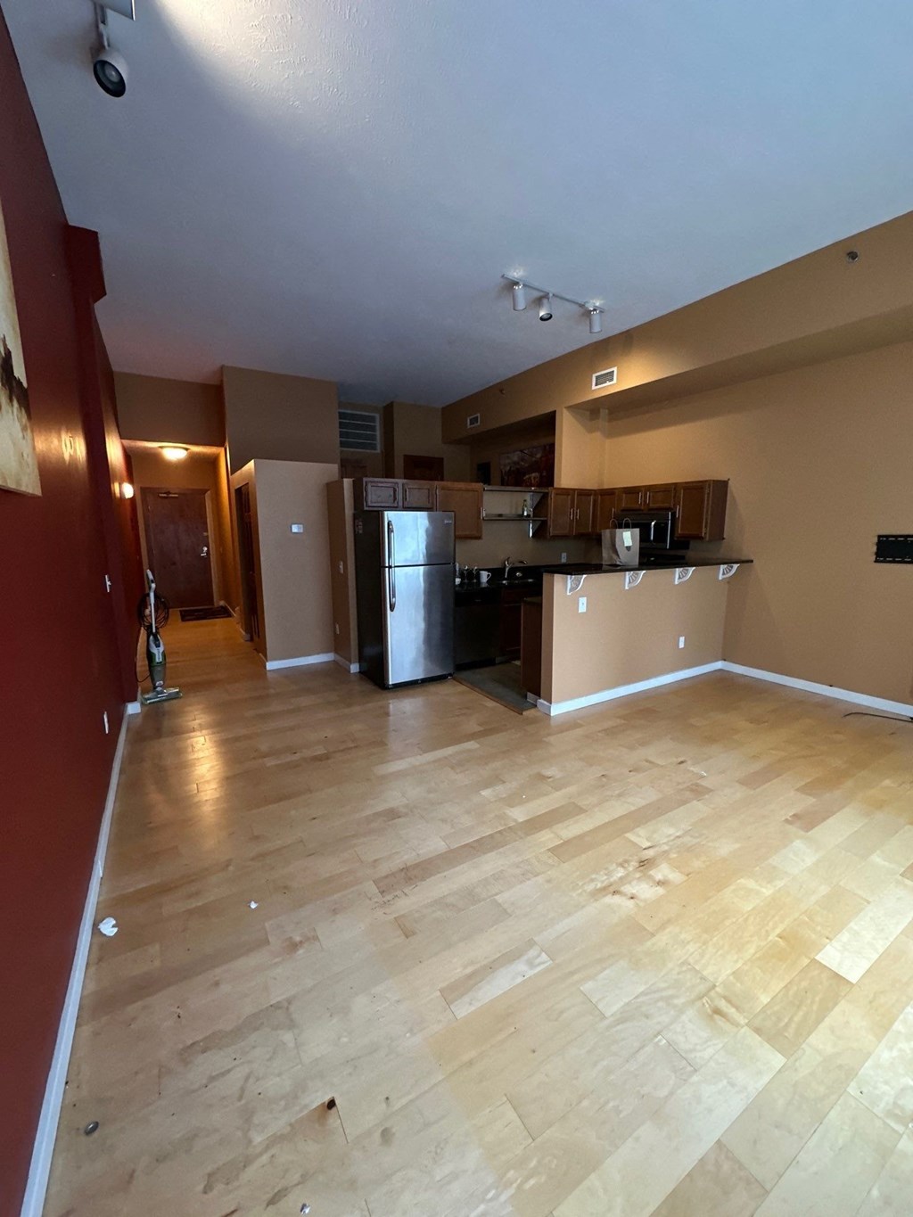 an empty living room with a kitchen and a wooden floor