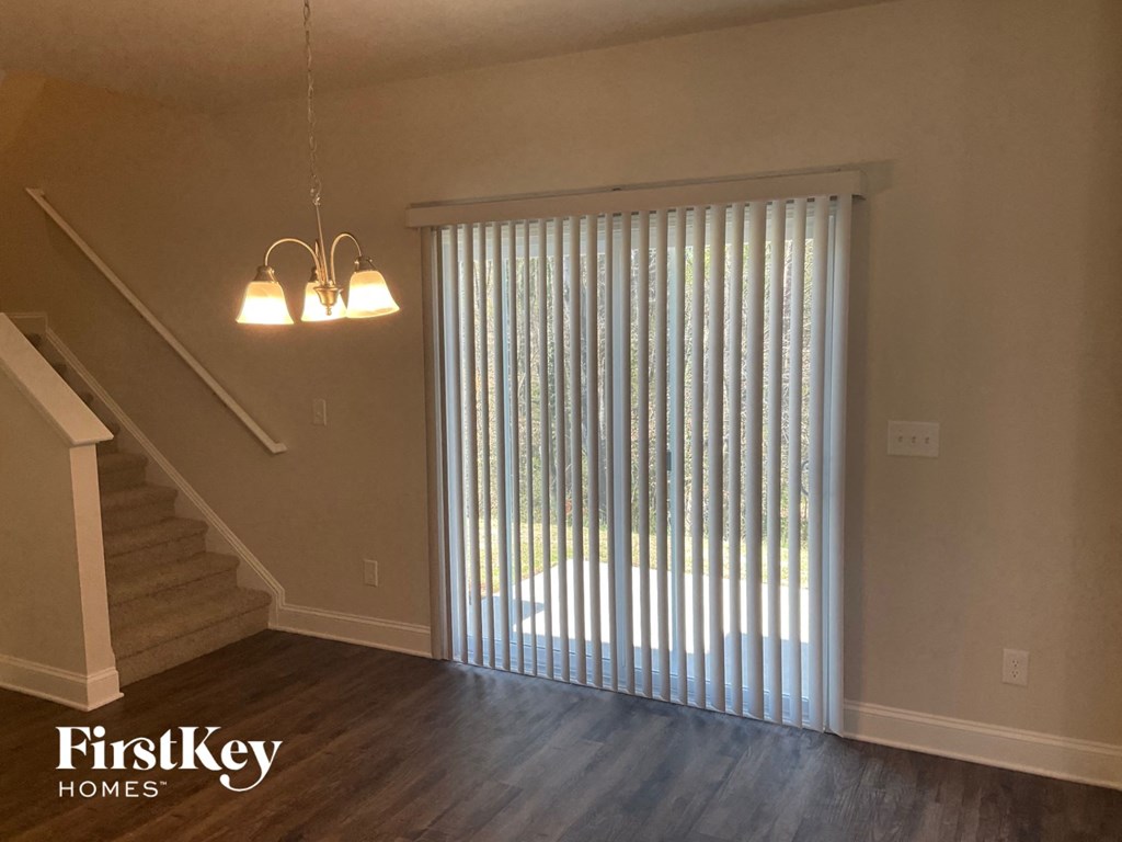 an empty living room with a staircase and a window with vertical blinds