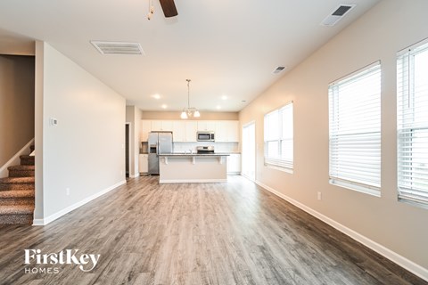 A spacious living room with a kitchen in the background and a staircase on the left.