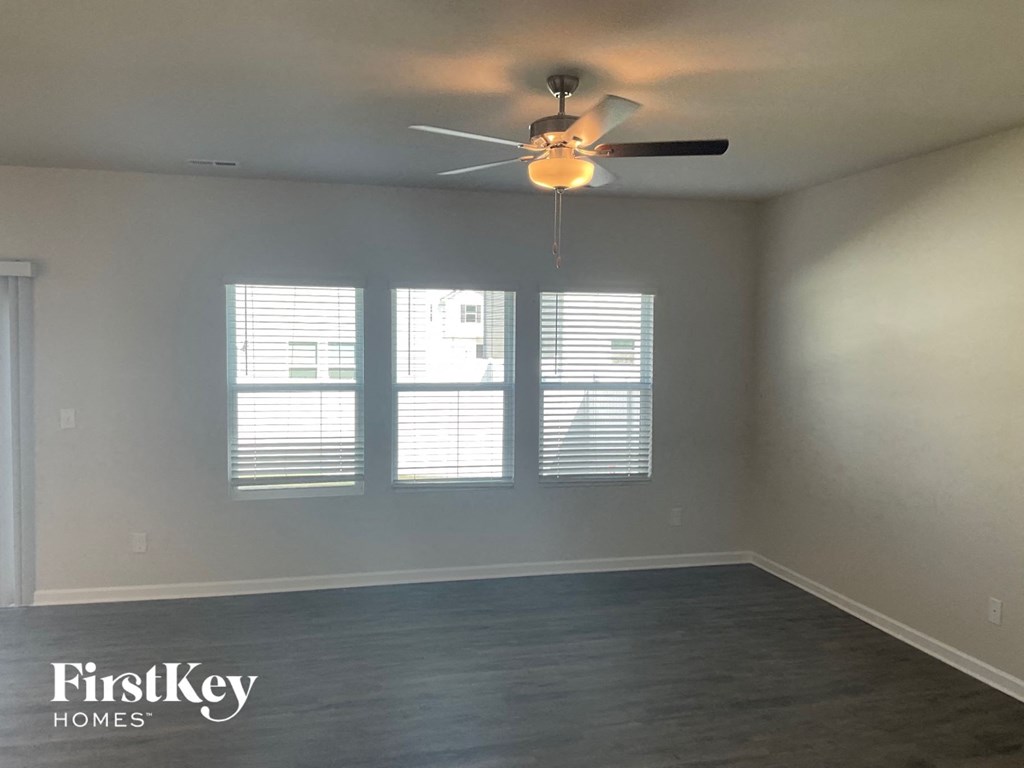 an empty living room with a ceiling fan and three windows