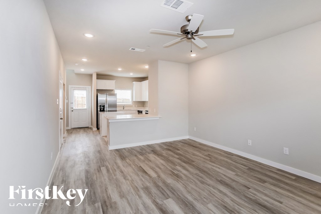 an empty living room with a ceiling fan and a kitchen