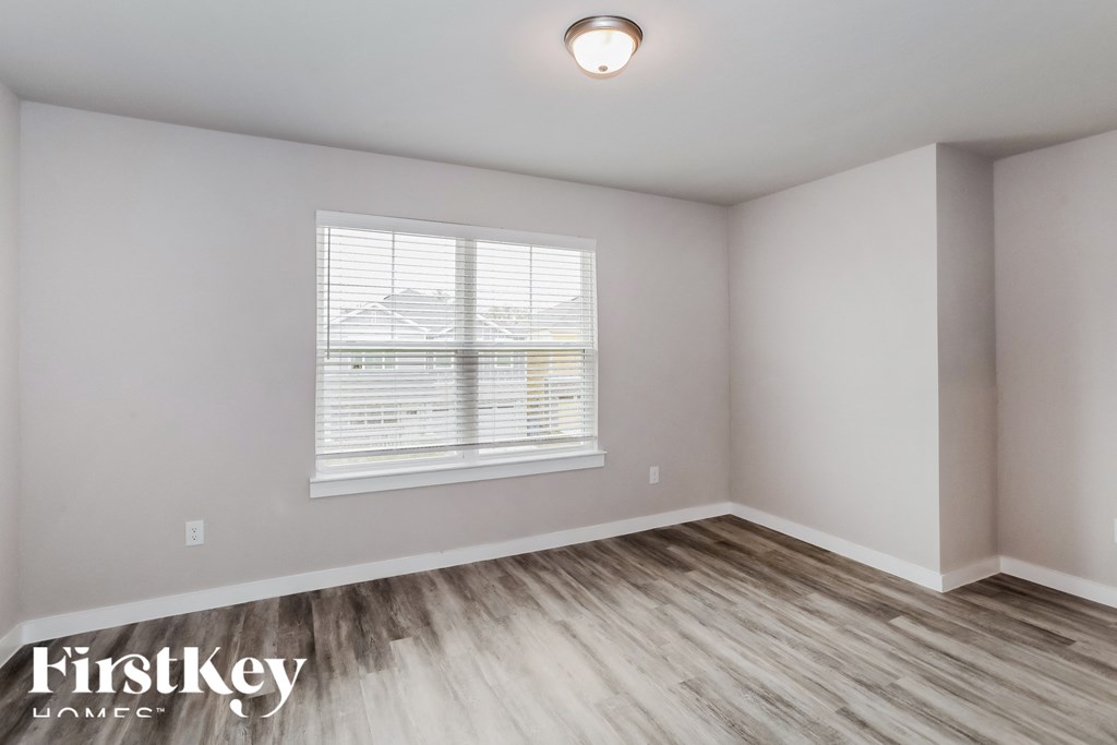 a bedroom with white walls and wood floors and a window