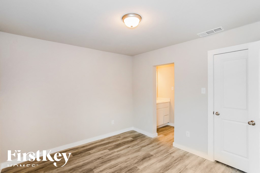 a bedroom with white walls and wood flooring and a door to a bathroom