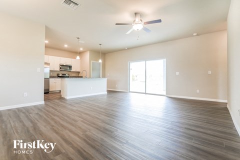 A spacious living room with a kitchen in the background and a ceiling fan above.