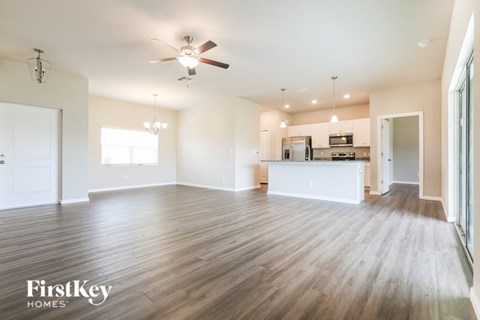 A spacious living room with a kitchen in the background and a ceiling fan above.