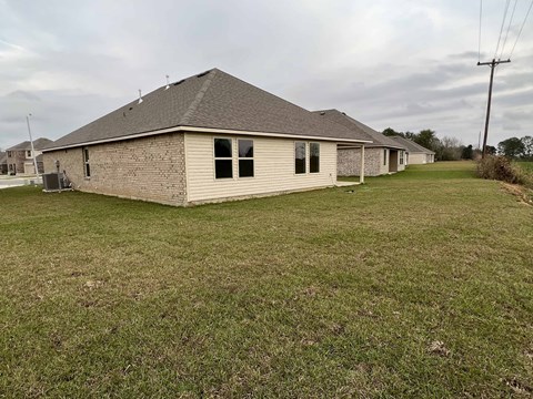 A house with a grey roof and a brown brick exterior sits in a grassy yard.