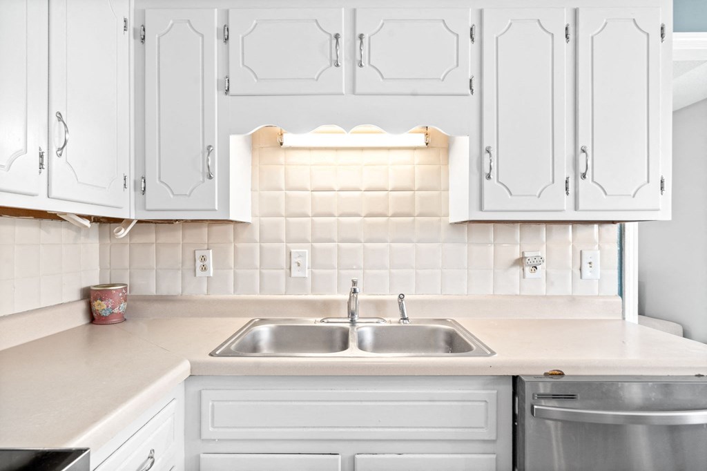 a white kitchen with white cabinets and a stainless steel sink