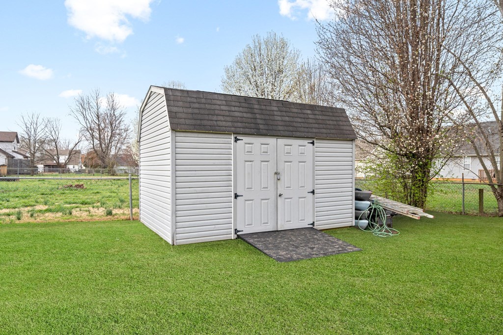 a shed with white doors and a black roof on a field