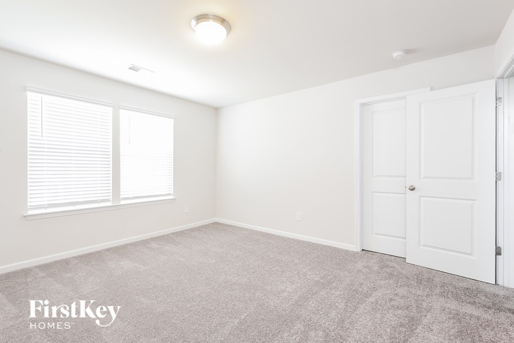 A room with a carpeted floor, a door, and a window with blinds.