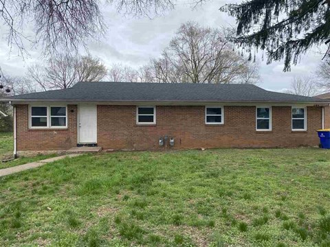 the front of a brick house with a lawn and trees