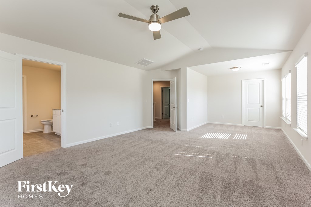 an empty living room with a ceiling fan and a door to a bathroom