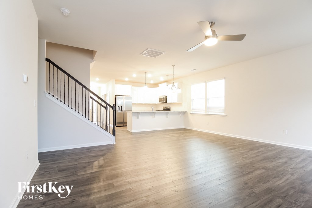 an empty living room and kitchen with wood floors and a ceiling fan