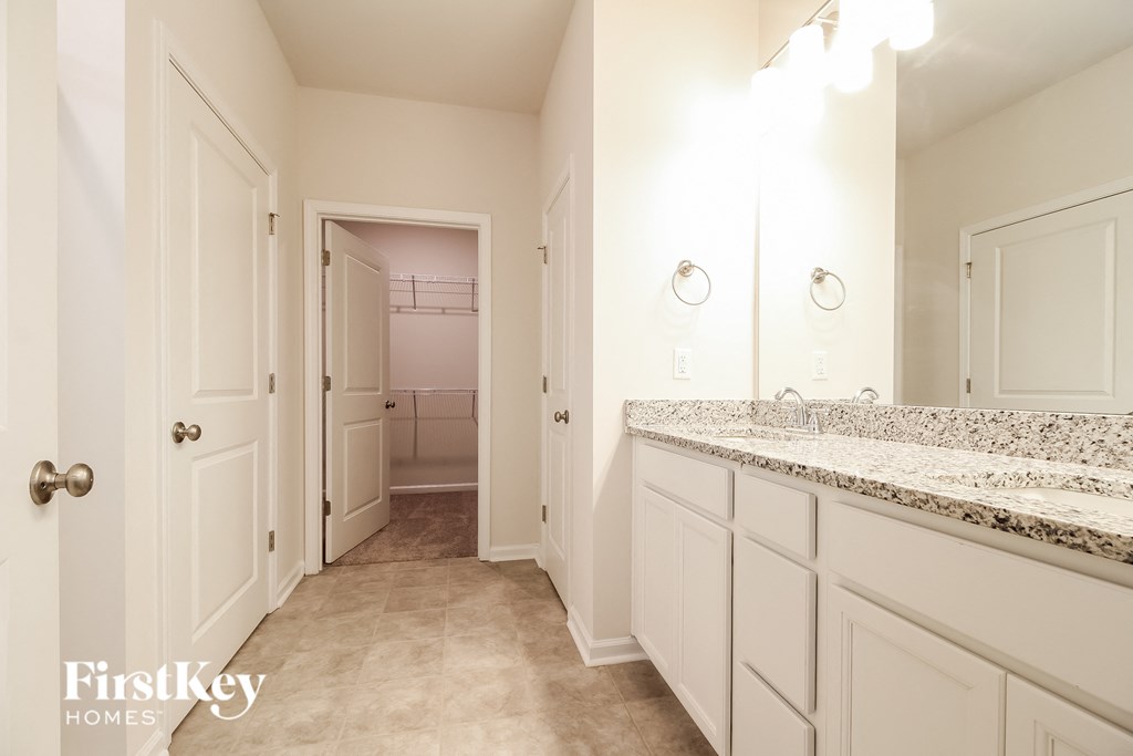a bathroom with white cabinets and granite counter tops and a hallway to a closet