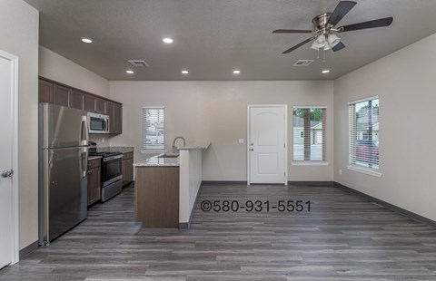 A well-lit, empty kitchen and living room with a wood floor and a ceiling fan.