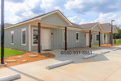 A small building with a grey and white exterior is surrounded by a concrete walkway.