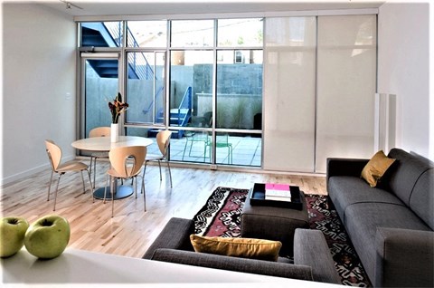 A living room with a grey couch, a white table, and a glass door leading to a balcony.