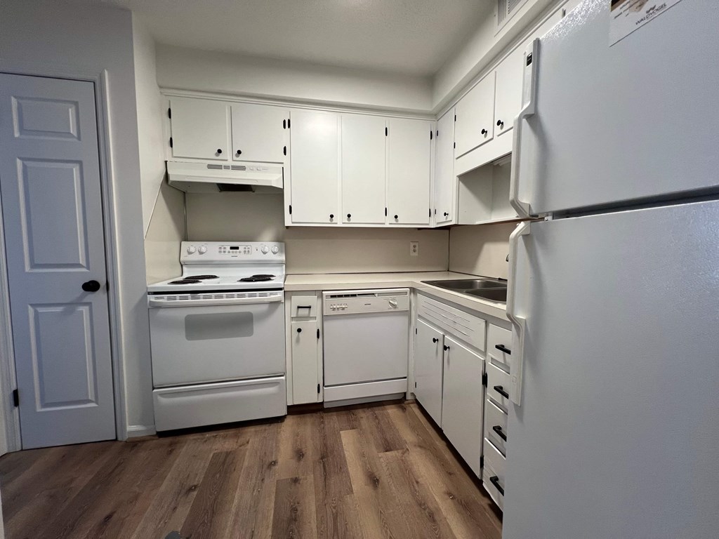 A kitchen with white appliances and wooden floors.