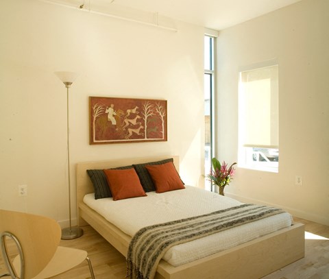 A bedroom with a bed, chair, and painting on the wall.