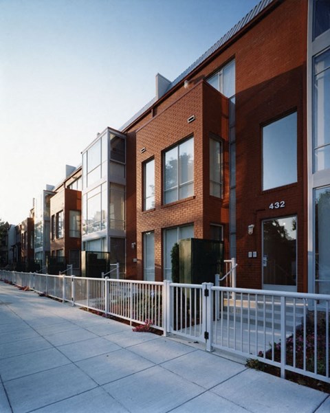 a row of brick buildings with a sidewalk and a white fence