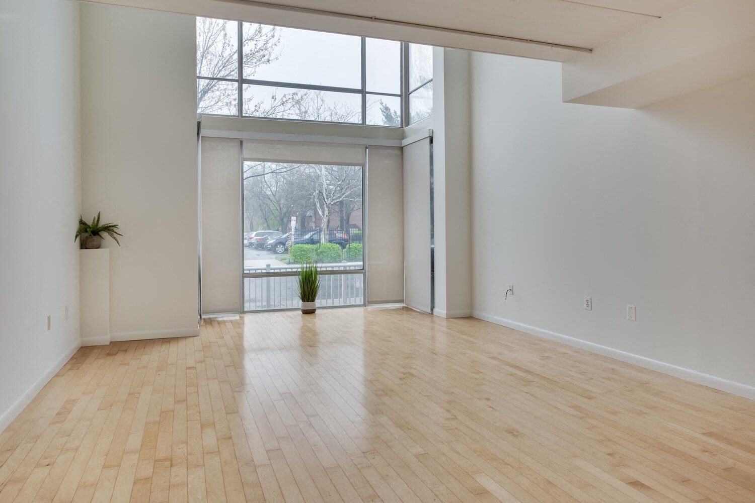 A room with wooden floors and a large window overlooking a yard.