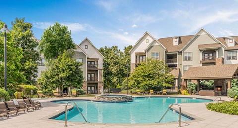 A large swimming pool in front of a two-story house with a deck and lounge chairs.