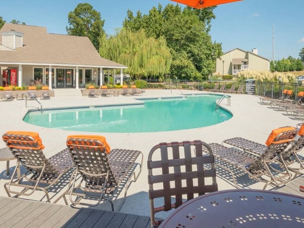 a swimming pool with chairs around it and a house in the background