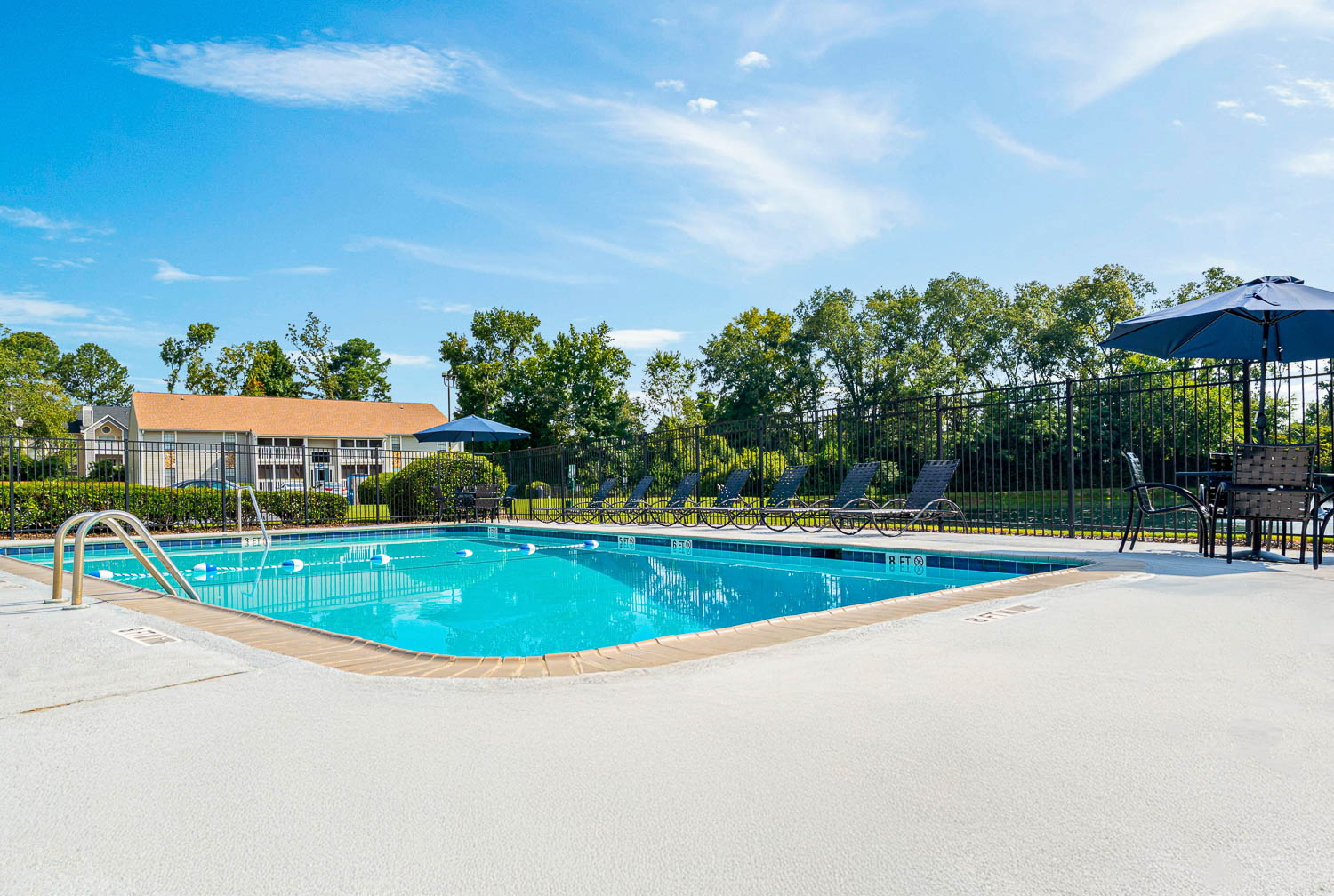 A large swimming pool with a blue sky and trees in the background.