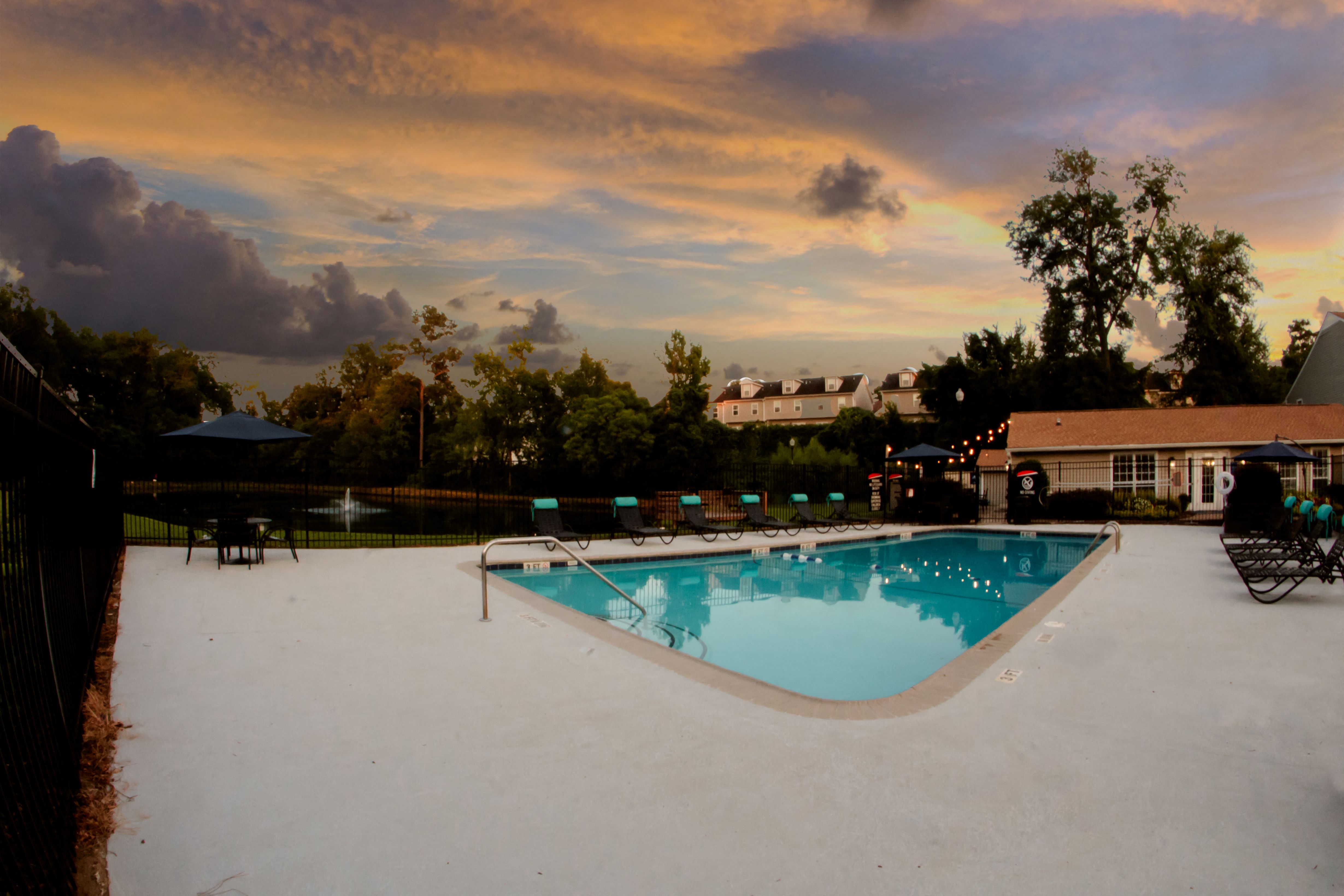 a swimming pool at sunset with a cloudy sky above it