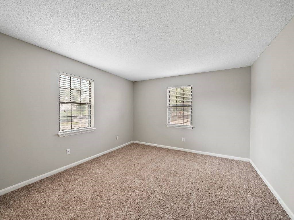 an empty bedroom with carpet and two windows
