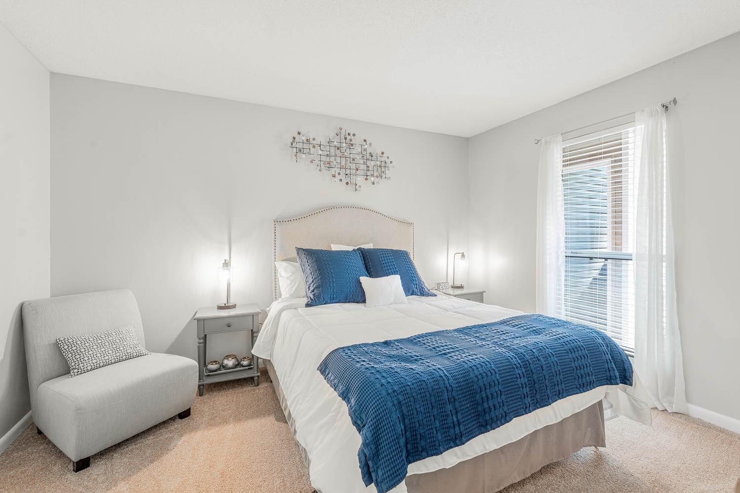 A bedroom with a bed, chair, and two lamps.