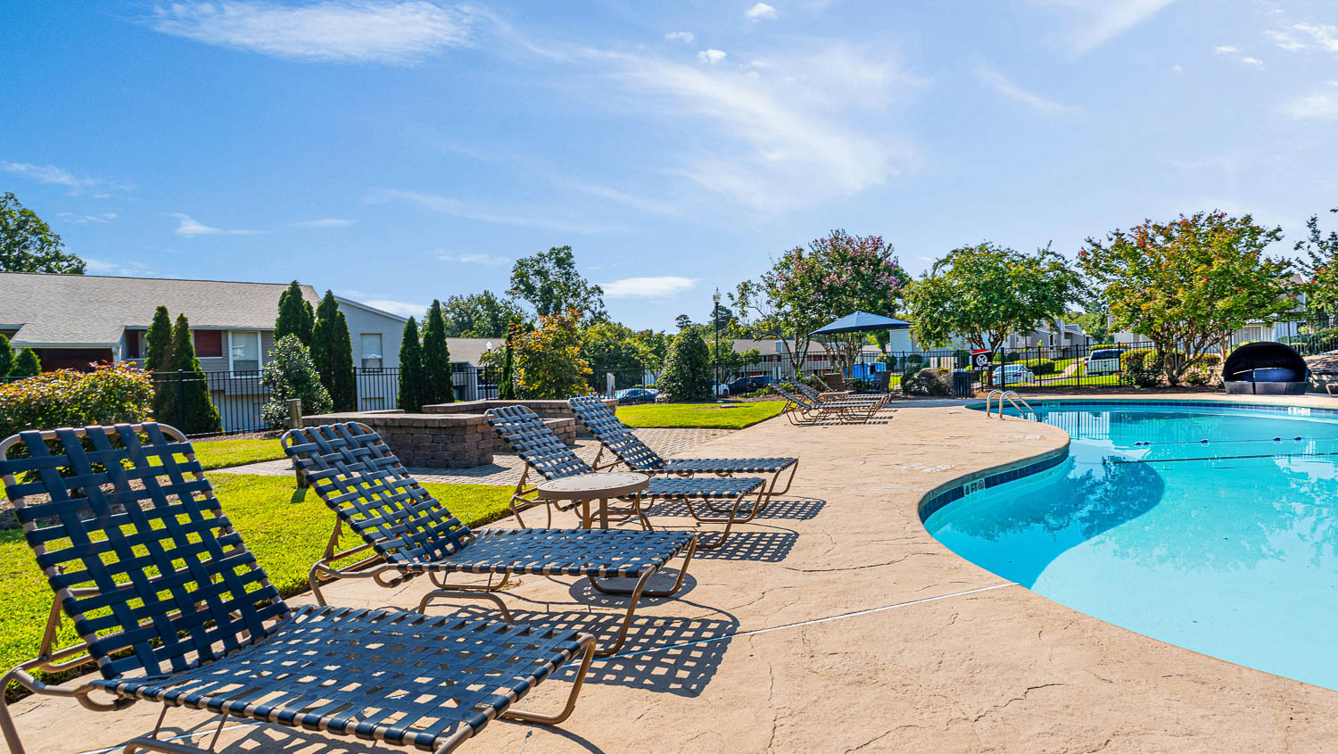 A pool surrounded by lawn chairs and trees.