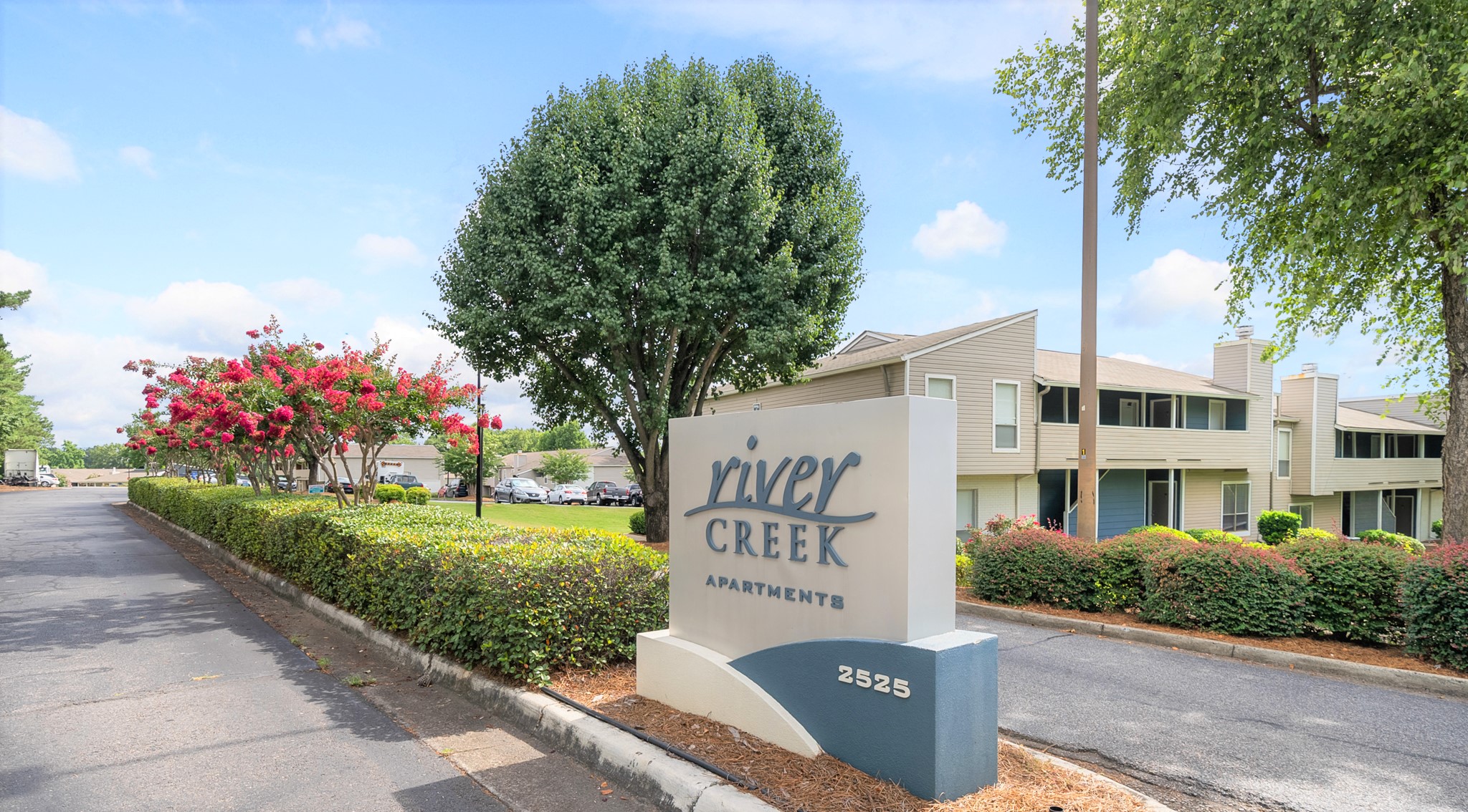 a sign for river creek apartments in front of trees and a street