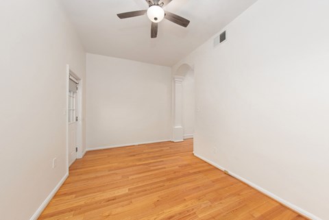 a living room with white walls and wood flooring and a ceiling fan