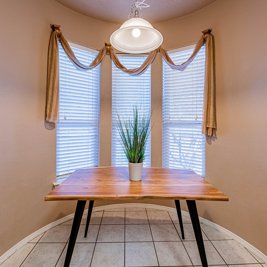 a dining room with three windows and a table with a plant