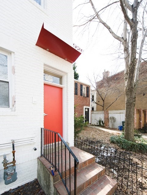 a red door on a white house next to a tree