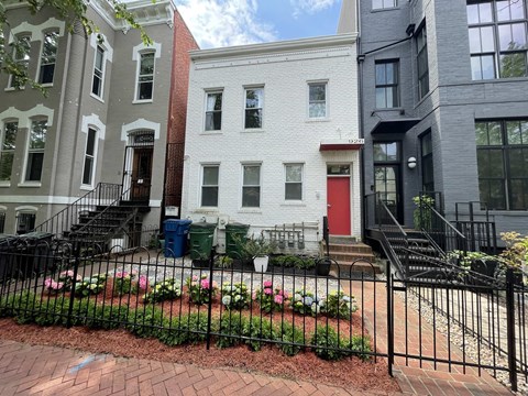 a white house with a red door behind a garden
