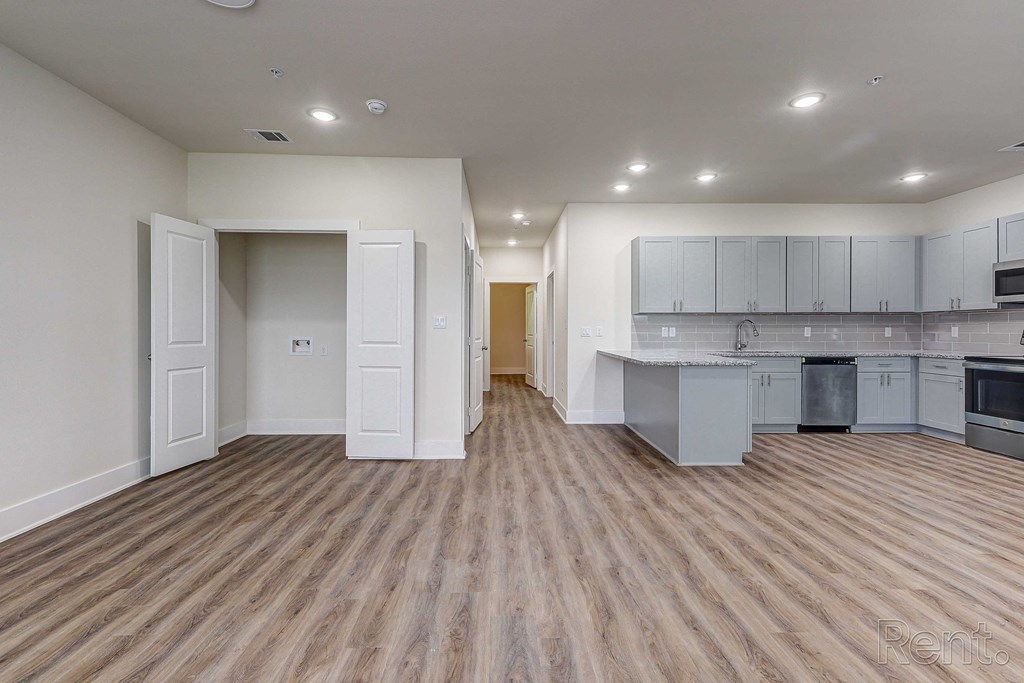 an empty living room and kitchen with white cabinets and wood flooring