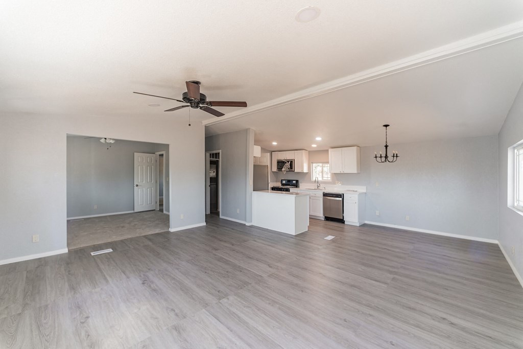 an empty living room with a ceiling fan and a kitchen